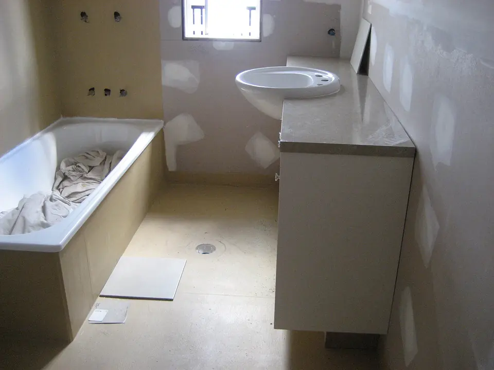 Salle de bain en rénovation avec baignoire et meuble vasque installés, murs en plaques de plâtre aux joints enduits encore à peindre.