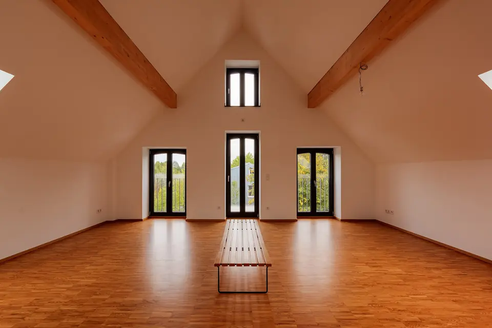 Combles aménagés en appartement dans une ancienne distillerie à Dülmen, avec parquet, murs blancs, poutres apparentes et portes-fenêtres sous le pignon.